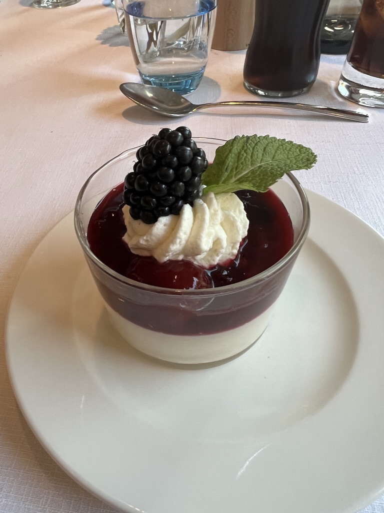 A layered dessert topped with cream, a blackberry and mint.