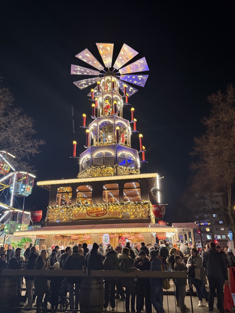 Illuminated Christmas pyramid above a busy market stall at night